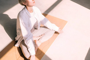 Eine Frau sitzt auf einer Yogamatte im Schneidersitz und meditiert.