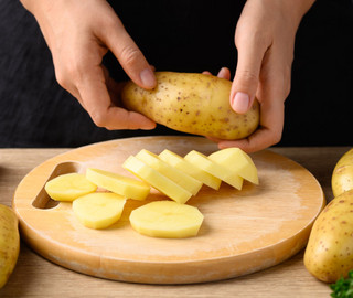 Kartoffelscheiben liegen auf einem Holzbrett, während eine Hand eine Kartoffel hält.