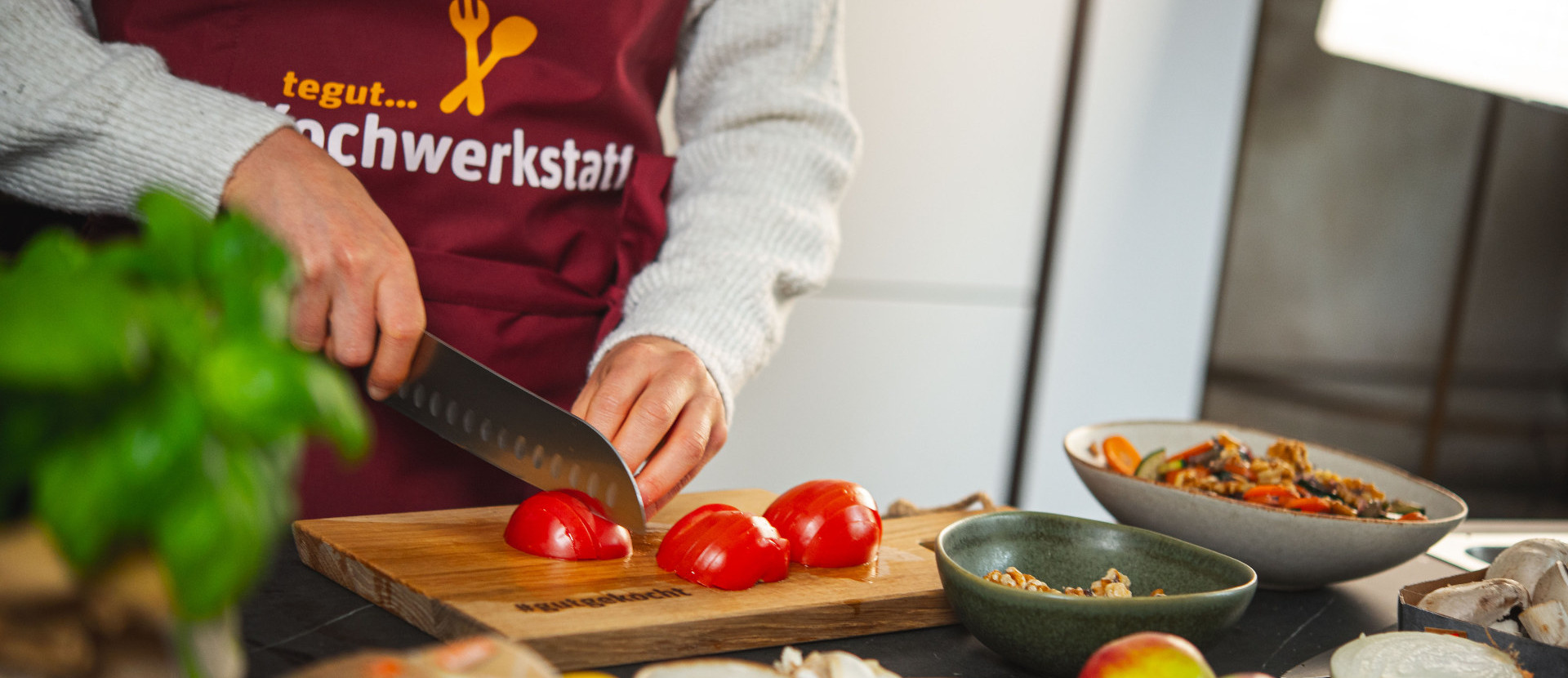Frau mit Kochwerkstatt-Schürze schneidet Tomaten in der Küche. 