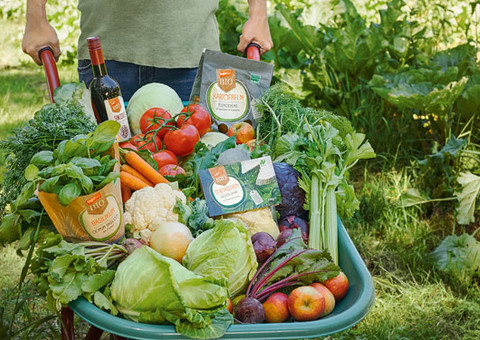 Das Bild symbolisiert die große Vielzahl an Bio-Produkten bei tegut: Ein Mann schiebt eine Schubkarre voll von frischem Obst und Gemüse sowie teguts Eigenmarken vor sich her.