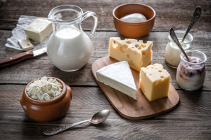 Verschiedene Käsesorten, Milch, Joghurt und Butter auf Holztisch angerichtet.