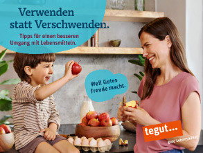Frau steht mit dem Kind in der Küche und schält einen Apfel