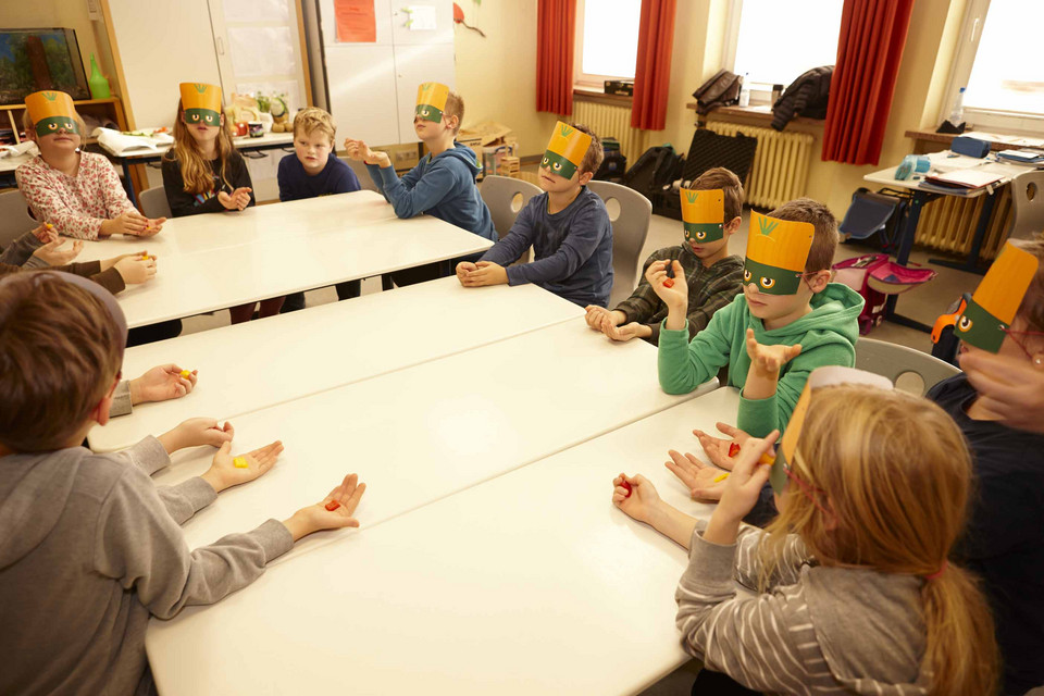 Kinder mit Masken sitzen an Tischen in der Schule und ertasten Lebensmittel