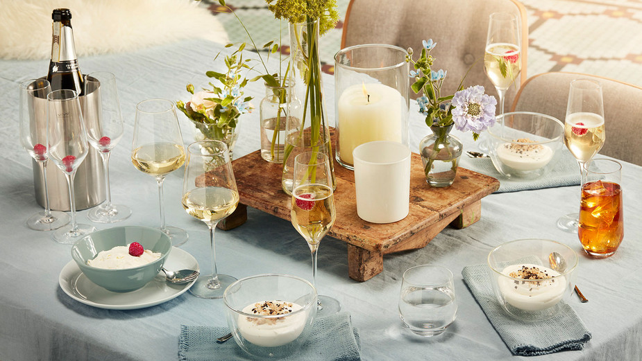 Gläser auf Tisch mit Nachtisch, Kerze, Blumen und Sekt