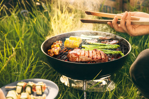 Nachhaltig grillen Grill mit Fleisch und Gemuese sowie Hand mit Grillzange