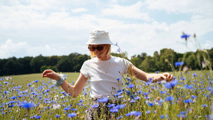 Junge Frau mit weißem T-Shirt, weißem Hut und Sonnenbrille in einem Meer aus blauen Kornblumen