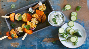 Vegane Grillspieße mit Tempeh, Süßkartoffeln und Zucchini an einem Dip aus Soja-Joghurt-Alternative und Gurken. Ein Symbolbild für vegan grillen.