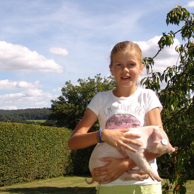 Mädchen hält Ferkel im Garten