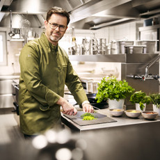 Jens Fischer vom Feldberghaus in Schmitten schneidet auf einem Brett gerade Gemüse, während er lächend in die Kamera schaut.