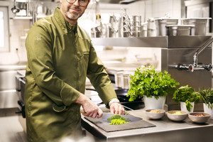 Jens Fischer vom Feldberghaus in Schmitten schneidet auf einem Brett gerade Gemüse, während er lächend in die Kamera schaut.