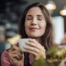 Eine Frau genießt gerade eine Tasse Kaffee und lächelt dabei zufrieden
