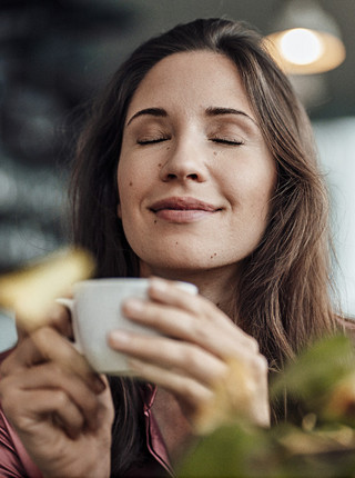 Eine Frau genießt gerade eine Tasse Kaffee und lächelt dabei zufrieden