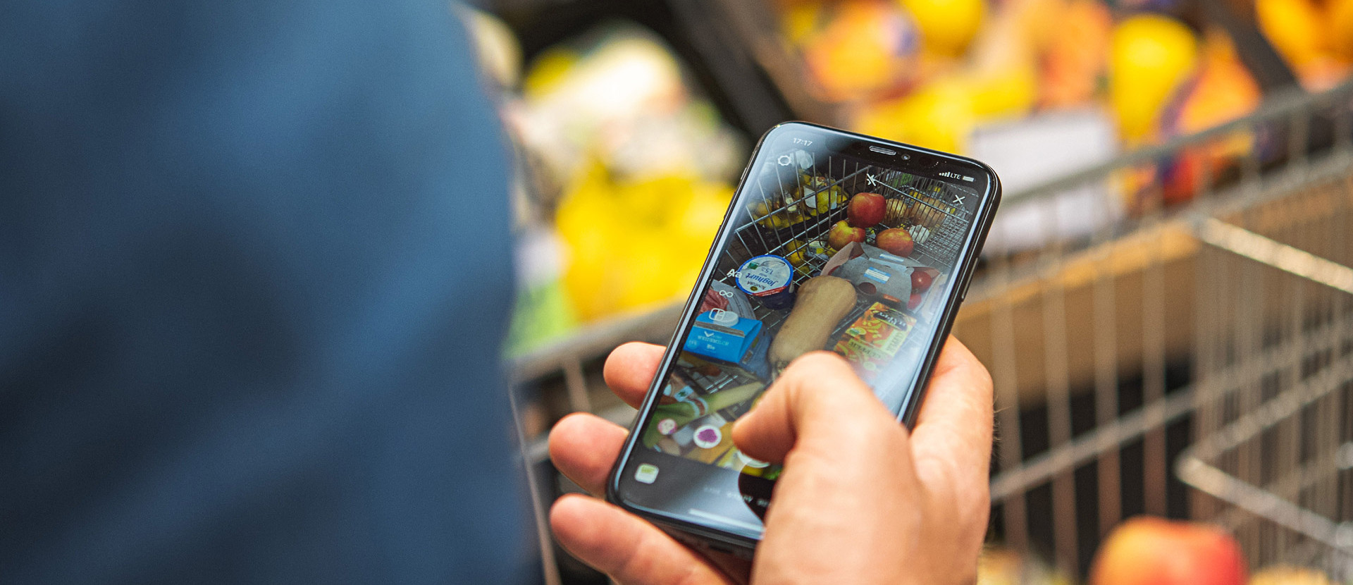 Ein Mann mit einem Smartphone in der Hand, der seine Einkäufe im Einkaufswagen fotografiert.