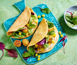 Drei Tacos mit Hühnchen, Avocado und Salat auf einem blauen Teller, dazu eine Schüssel mit Gemüse auf einer grün strukturierten Oberfläche.