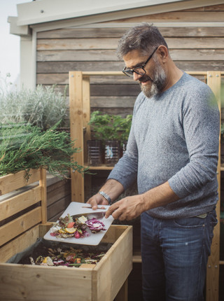 Ein Mann steht auf seiner Terasse und schüttet Lebensmittelreste in seinen Kompost.