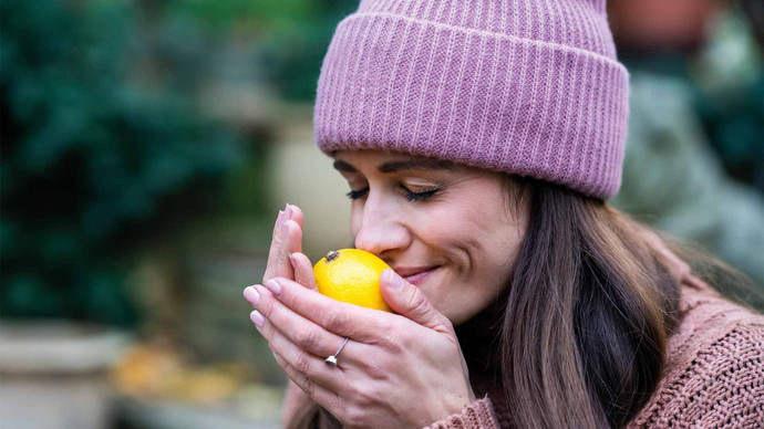 Eine Frau mit Mütze, die an einer Zitrone riecht und bewusst das Aroma genießt.