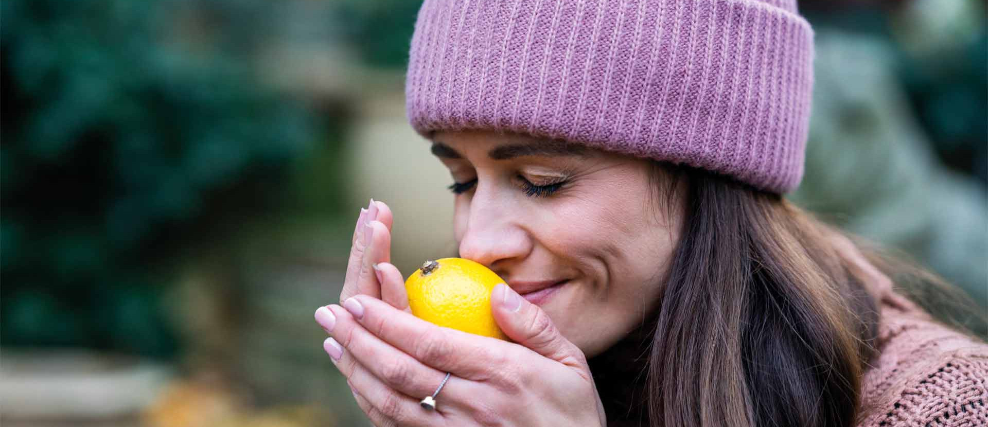 Frau mit Mütze riecht an einer Zitrone in ihren Händen