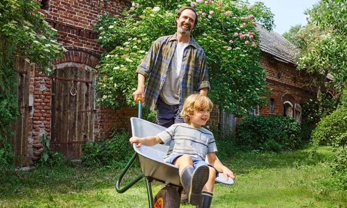 40 Jahre Bio bei tegut. Für dieses Symbolbild schiebt ein Vater in der Schubkarre seinen Jungen im Garten. Beide lachen.