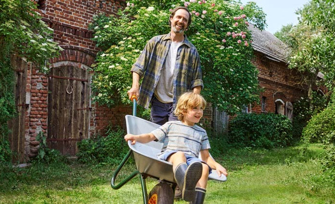 40 Jahre Bio bei tegut. Für dieses Symbolbild schiebt ein Vater in der Schubkarre seinen Jungen im Garten. Beide lachen.