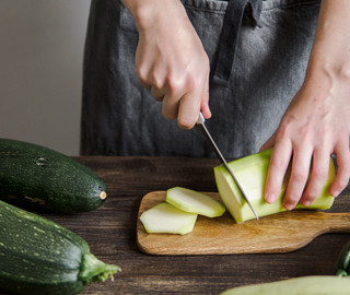 Eine Frau schneidet auf einem Küchenbrett eine Zucchini in Stücke