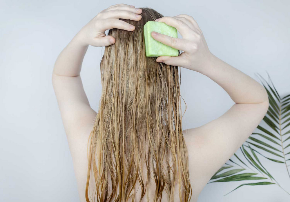Frau mit langen blonden Haaren und festem Shampoo unter der Dusch 