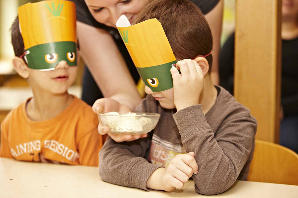 Junge mit Maske vor den Augen riecht an Lebensmitteln in einer Schüssel