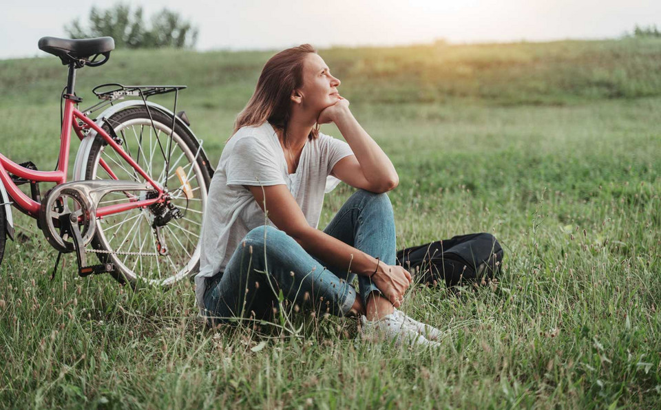 Frau sitzt in einer Wiese mit Fahrrad im Hintergrund