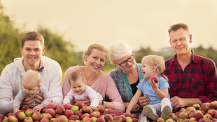 Die Familie Münch, vier Erwachsene und drei Kleinkinder, posieren hinter mit Äpfeln aufgeschütteten Kisten