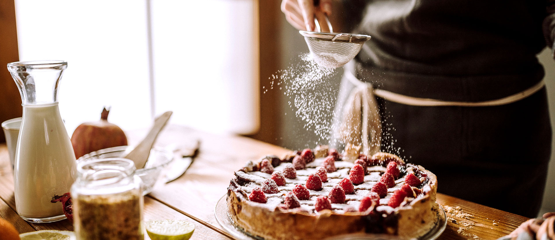 Hand streut mit Sieb Zucker ueber Kuchen