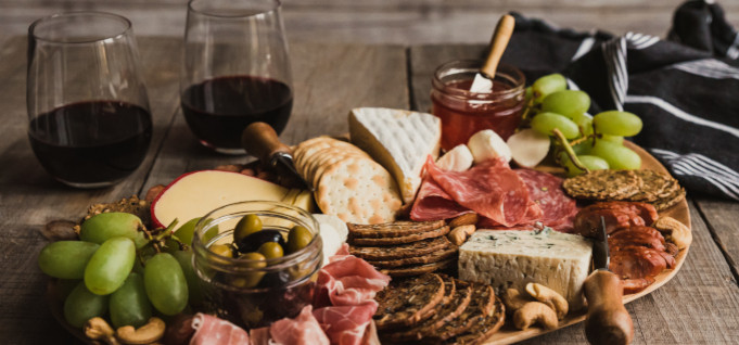 Mehrere Lebensmittel wie Salami, Schinken, Käse, Oliven auf Holzbrett.
