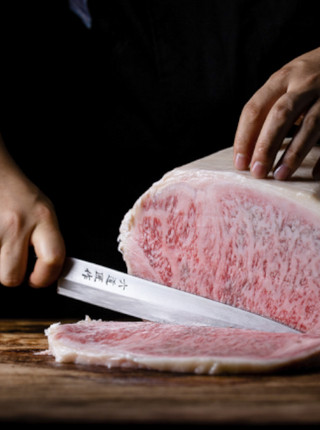Wagyu Beef mit einer feinen Marmorierung wird mit einem großen Messer in zarte Streifen geschnitten.