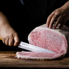 Wagyu Beef mit einer feinen Marmorierung wird mit einem großen Messer in zarte Streifen geschnitten.