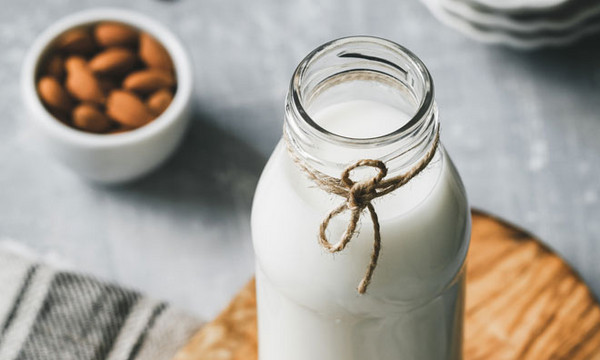 veganer Milchersatz Milchflasche neben Schüssel mit Mandeln