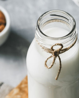 veganer Milchersatz Milchflasche neben Schüssel mit Mandeln