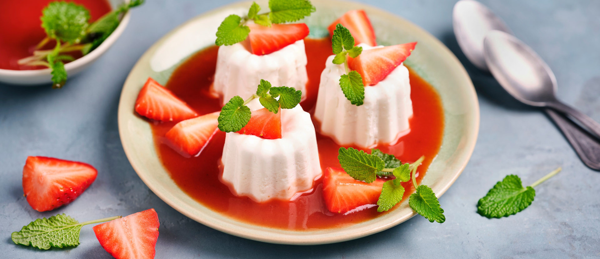 vegane Erdbeer Panna Cotta mit roter Erdbeersauce präsentiert auf einem weißem Teller