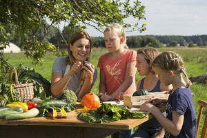 Eine Mutter mit Ihren 3 Töchtern sitzen an einem Tisch im Garten, während sie zusammen Gemüse schneiden