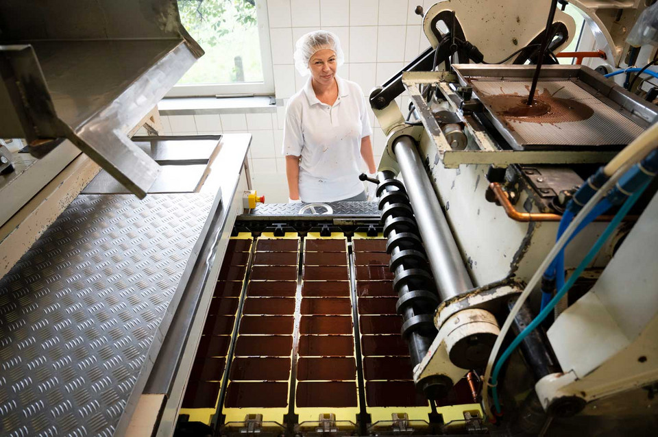 Frau an großer Maschine, die Schokolade produziert
