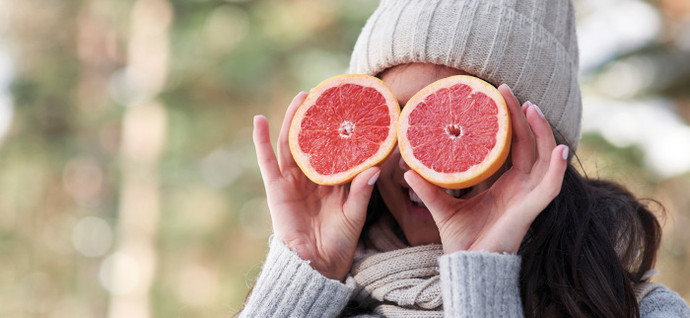 Eine Frau hält sich zwei halbierte Grapefruits vor die Augen