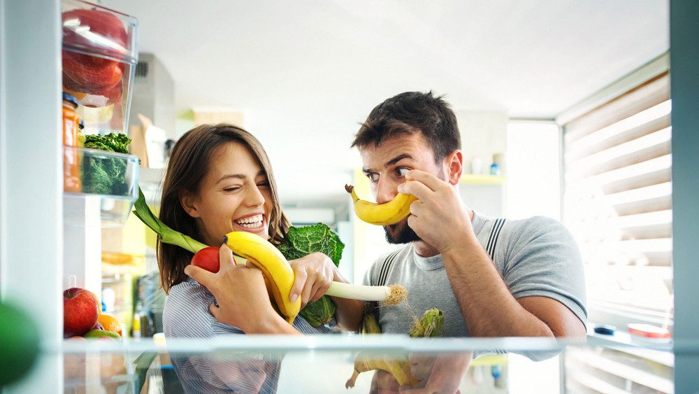 Mann und Frau stehen vor Kühlschrank mit Obst und Gemüse