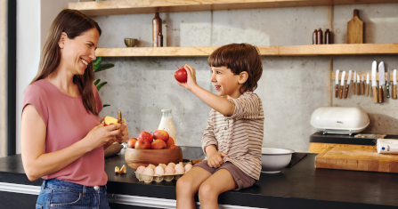 Eine Frau steht mit Ihrem Sohn in der Küche, während der Sohn einen Apfel in der Hand hält