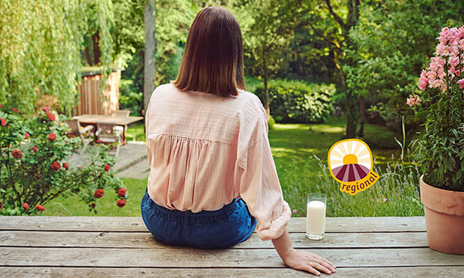 Regionale Produkte Frau sitzt auf Holzterrasse mit Glas Milch