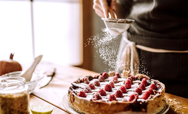 Backen ohne Zucker: Das Bild zeigt einen Kuchen, der gerade über ein Sieb mit einer Zuckeralternative bestreut wird.