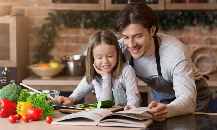 Vater und Tochter stehen gemeinsam in der Küche und schauen sich ein Kochbuch an