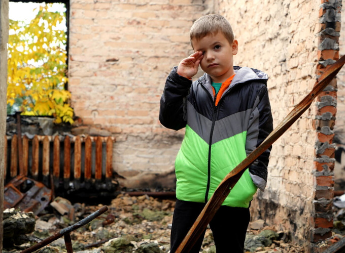 Ein kleiner Junge steht in den Trümmern eines Hauses, während er sich die Augen reibt