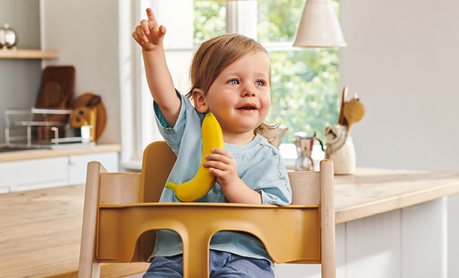 kleines Mädchen sitzt Banane in einem Hochstuhl