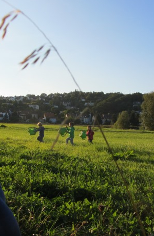 Drei Kinder laufen über ein Feld mit Gießkannen in der Hand
