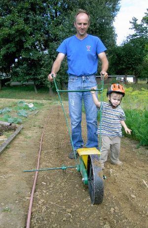Ein Mann mit einem Kind laufen mit einem Gartenwerkzeug auf dem Acker