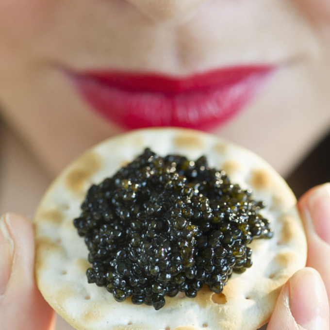 Einer Frau hält Kaviar vor sich. Im Hintergrund sieht man nur ihren Mund mit einem leichten lächeln auf den Lippen