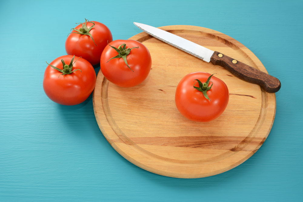 Messer und vier Tomaten auf Holzbrett