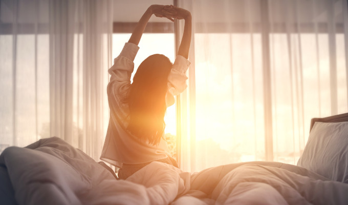 Eine Frau streckt sich im Bett, während der Sonnenaufgang in Ihr Zimmer scheint
